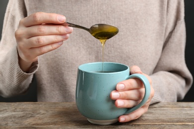 Photo of Woman putting honey into tea at wooden table, closeup