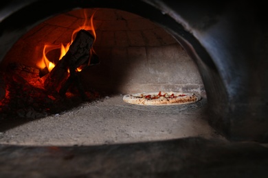 Photo of Burning firewood and tasty pizza in oven at restaurant kitchen