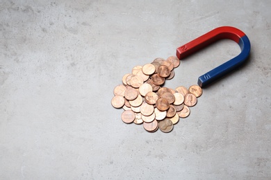Photo of Magnet attracting coins on grey background, space for text. Business concept