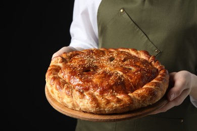 Photo of Woman holding tasty homemade pie on black background, closeup