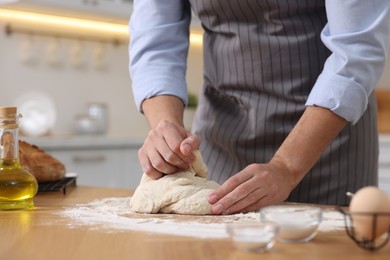 Photo of Making bread. Man kneading dough at wooden table in kitchen, closeup
