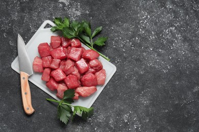 Photo of Cooking delicious goulash. Raw beef meat, parsley and knife on grey textured table, flat lay. Space for text