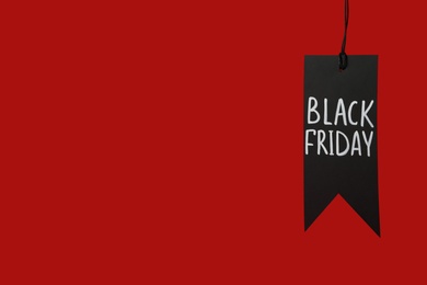 Photo of Tag with phrase Black Friday on red background, space for text