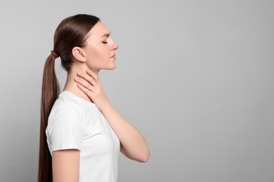 Photo of Young woman with sore throat on light grey background. Space for text