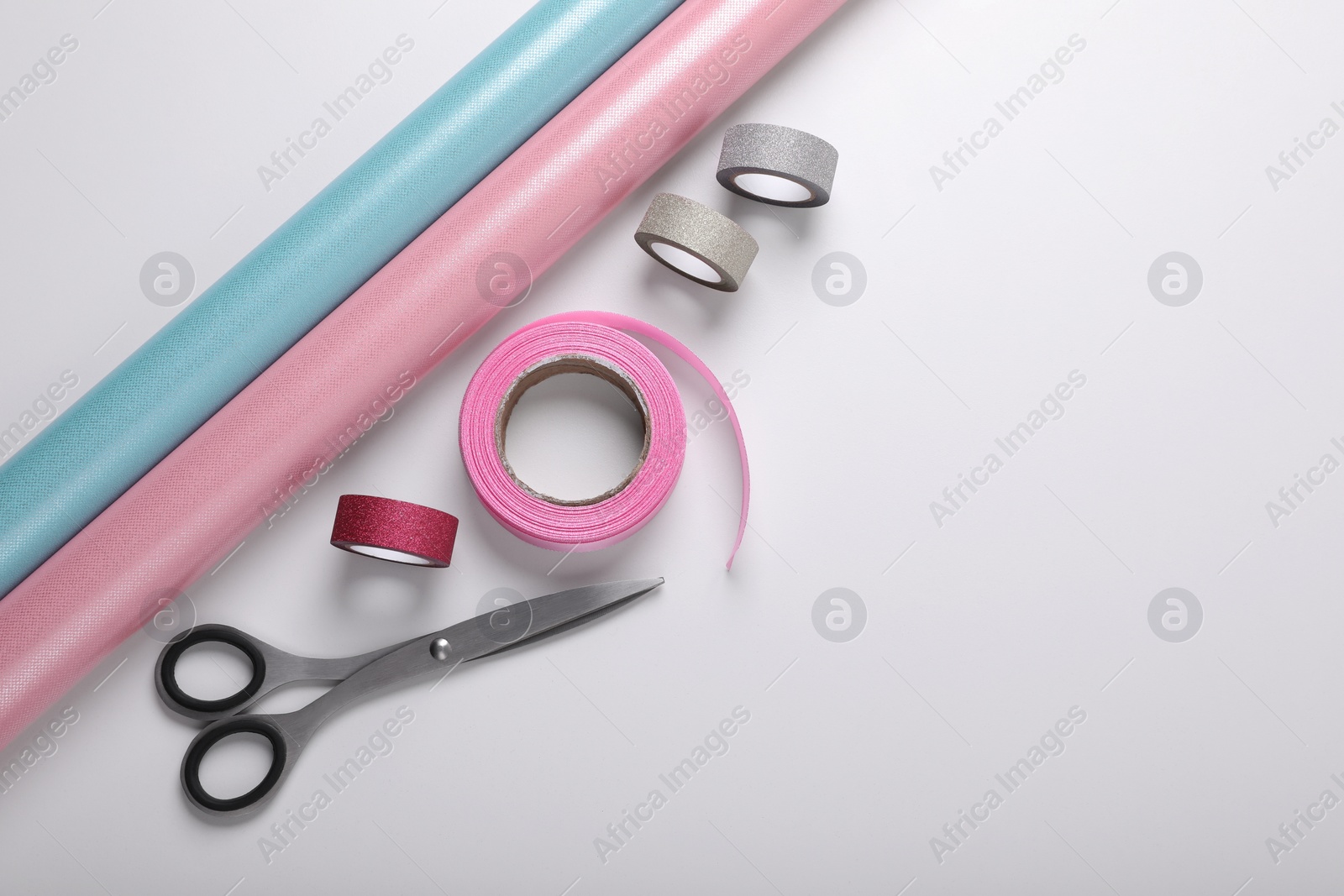 Photo of Rolls of colorful wrapping papers, scissors and ribbons on white background, flat lay. Space for text
