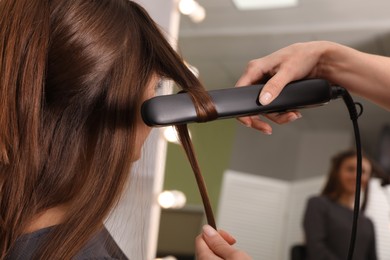 Photo of Stylist curling woman's hair with flat iron in salon