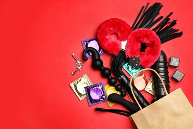Photo of Shopping bag and different sex toys on red background, flat lay. Space for text