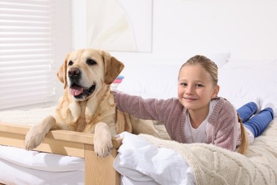 Photo of Cute child with her Labrador Retriever on bed at home. Adorable pet