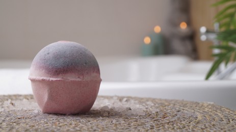 Photo of Beautiful bath bomb on wicker mat in bathroom, space for text