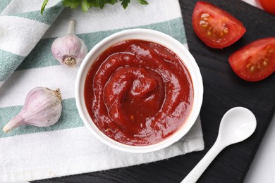 Photo of Organic ketchup in bowl, fresh tomatoes and garlic on table, flat lay. Tomato sauce