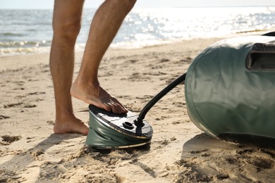 Photo of Man pumping inflatable rubber fishing boat at sandy beach on sunny day, closeup
