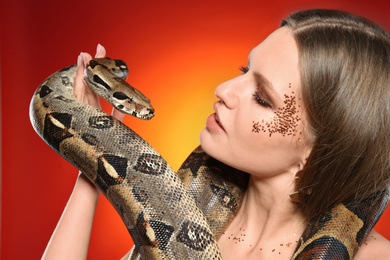 Photo of Beautiful woman with boa constrictor on bright colorful background, closeup