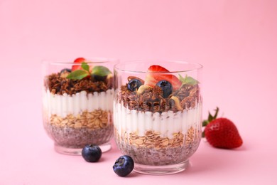 Photo of Tasty granola with berries, nuts, yogurt and chia seeds in glasses on pink background