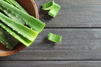 Photo of Bowl of fresh aloe vera leaves on wooden table, flat lay composition with space for text