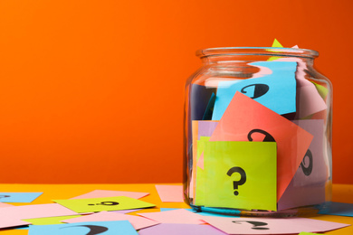 Photo of Colorful cards with question marks in glass jar on orange background. Space for text