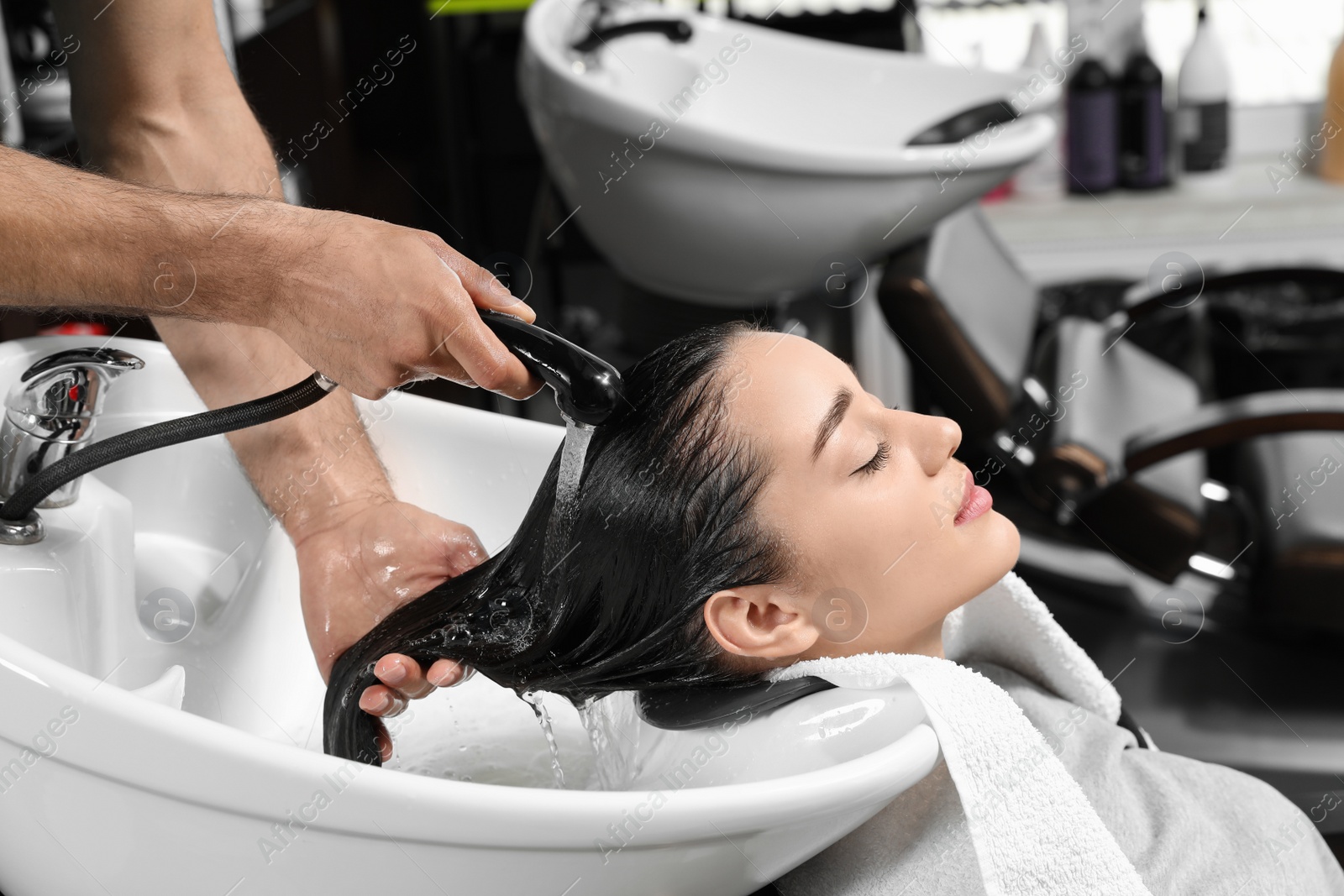 Photo of Stylist washing client's hair at sink in beauty salon