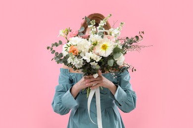 Photo of Woman covering her face with bouquet of beautiful flowers on pink background