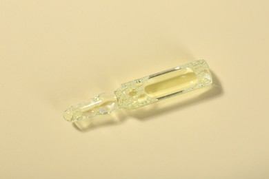 Photo of Glass ampoule with liquid on beige background, top view