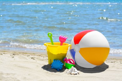 Set of plastic beach toys and inflatable ball on sand near sea. Space for text