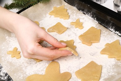 Photo of Woman putting raw Christmas cookies on baking tray at table, closeup