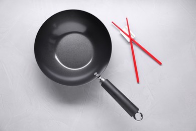 Photo of Empty iron wok and chopsticks on grey table, flat lay