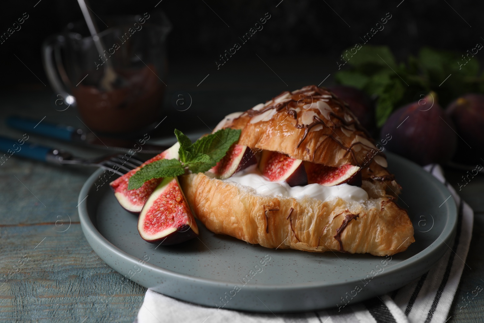 Delicious croissant with figs and cream served on light blue wooden table Photo of Delicious croissant with figs and cream served on light blue wooden table