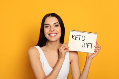 Photo of Happy woman holding notebook with words Keto Diet on yellow background