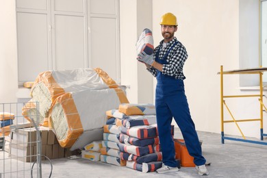 Photo of Professional builder in uniform with bag of cement indoors