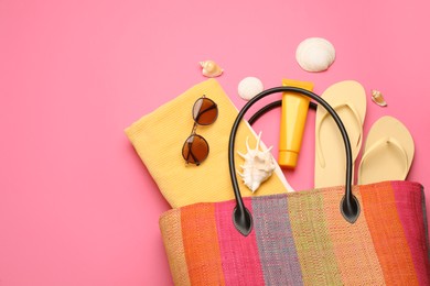 Photo of Stylish bag with beach accessories on pink background, flat lay