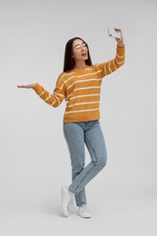 Photo of Smiling young woman taking selfie with smartphone on white background