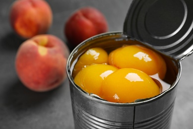 Photo of Tin can with conserved peach halves on table, closeup