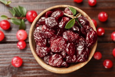 Photo of Tasty dried cranberries in bowl, fresh ones and leaves on wooden table, top view