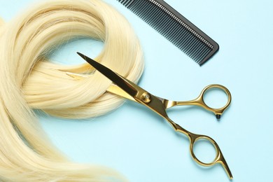 Photo of Professional hairdresser scissors and comb with blonde hair strand on light blue background, flat lay