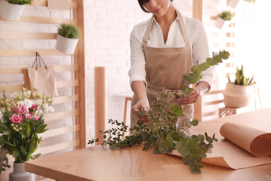 Photo of Florist making beautiful bouquet at table in workshop, closeup