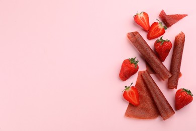 Photo of Delicious fruit leather rolls and strawberries on pink background, flat lay. Space for text