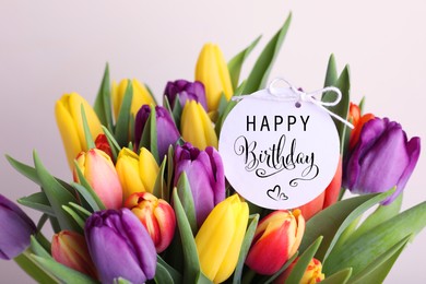 Image of Beautiful bouquet of tulip flowers with Happy Birthday card on light background, closeup