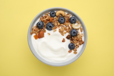 Photo of Bowl with yogurt, blueberries and granola on yellow background, top view