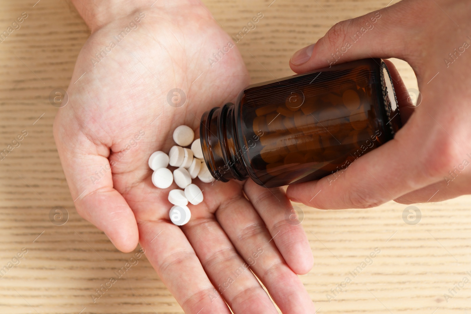Man pouring pills from bottle at wooden table, top view Photo of Man pouring pills from bottle at wooden table, top view
