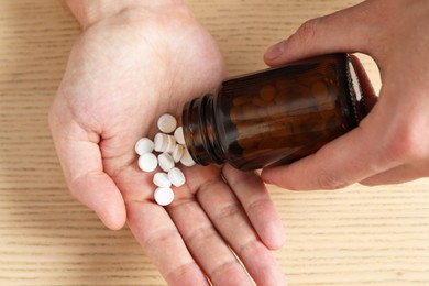 Photo of Man pouring pills from bottle at wooden table, top view