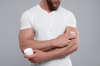 Photo of Man applying body cream onto his arm on light grey background, closeup