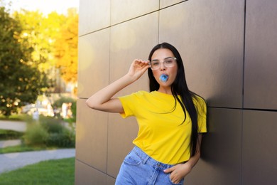 Photo of Beautiful woman blowing gum near dark tiled wall outdoors, space for text