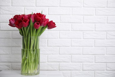 Photo of Bouquet of beautiful tulips in glass vase on white table indoors. Space for text