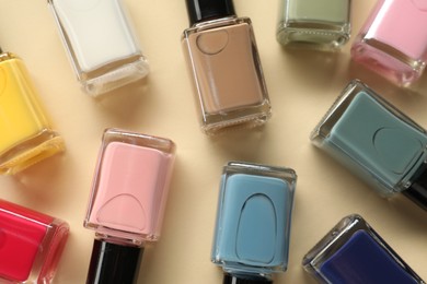 Photo of Colorful nail polishes in bottles on beige background, flat lay