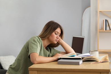 Photo of Sleepy young woman studying at wooden table indoors