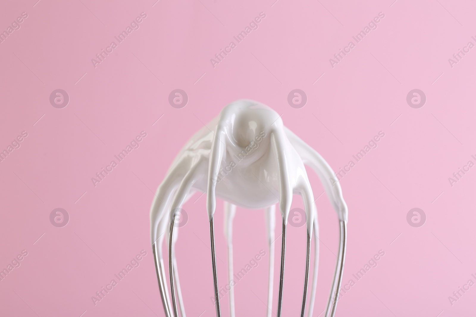 Photo of Whisk with whipped cream on pink background, closeup