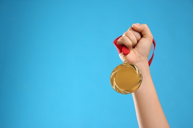 Photo of Woman holding gold medal on light blue background, closeup. Space for text
