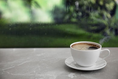 Photo of Cup of hot drink on stone windowsill against glass with rain drops, space for text