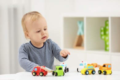 Photo of Children toys. Cute little boy playing with toy cars at white table in room, space for text