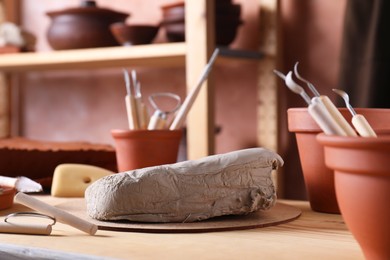 Photo of Clay and set of modeling tools on wooden table in workshop, closeup