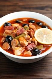 Photo of Meat solyanka soup with sausages, olives and vegetables on wooden table, closeup